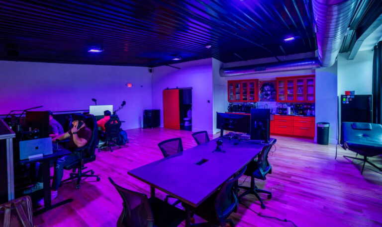 Sanctum Studio conference and podcast recording room with large table, ergonomic chairs, red cabinetry, and purple LED lighting in Roanoke TX