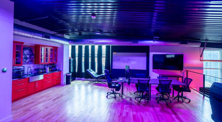 Sanctum Studio open coworking and lounge area with red cabinetry, large TV display, hardwood floors, and purple ambient lighting in Roanoke TX