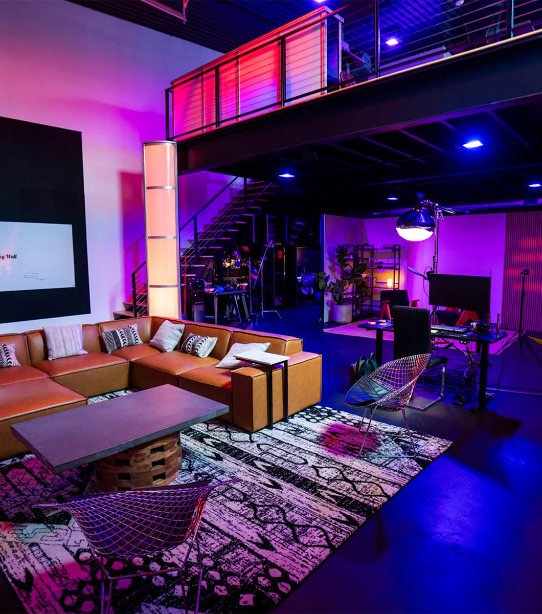 Sanctum Studio lounge area in Roanoke TX with leather sectional sofa, colorful area rug, and two-story mezzanine lit with purple and red LED lighting