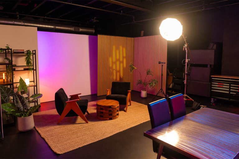 Sanctum Studio styled interview set with two chairs, wood coffee table, acoustic slat wall panels, large studio light, and pink-purple LED backdrop in Roanoke TX